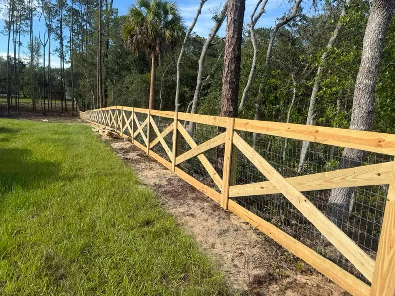 Crossbuck wood ranch fence with welded wire backing running along a wooded Florida property line